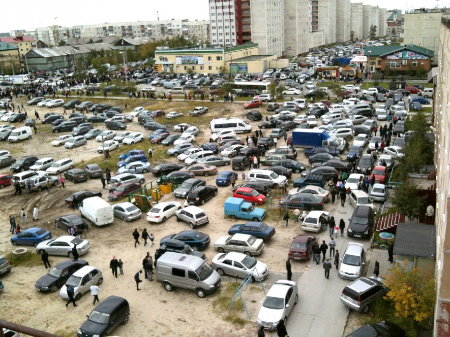 Необустроенная парковка с хаотично стоящими автомобилями Необустроенная парковка с хаотично стоящими автомобилями
