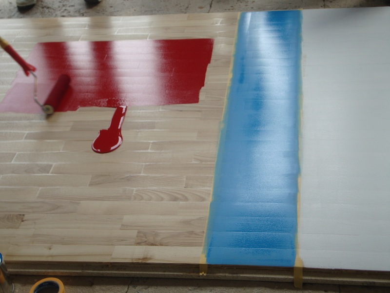 Нанесение спортивной разметки красного цвета на игровом поле Нанесение спортивной разметки красного цвета на игровом поле